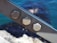 Three metal hexagonal bolts are fastened on a steel beam with an out-of-focus background of blue water and rocks.