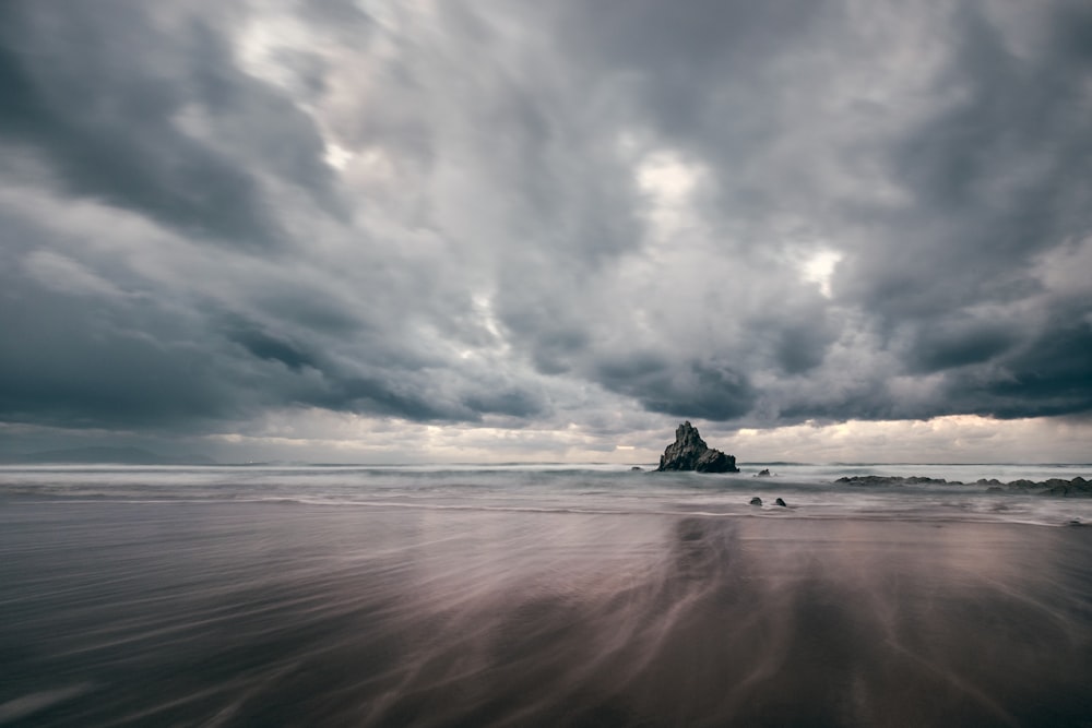 black rock formation on sea under gray clouds