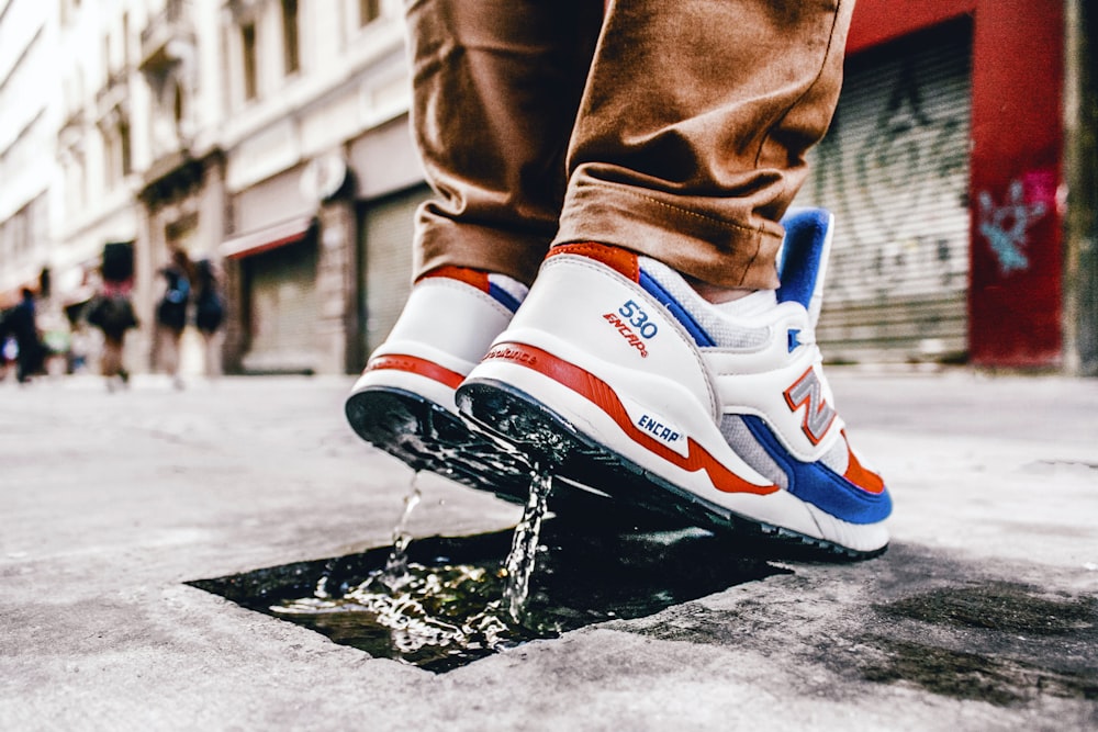 Person wearing pair of white-blue-and-orange New Balance 530 sneakers on  gray road photo – Free São paulo Image on Unsplash