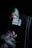 A person with light-colored hair holds a tarot card labeled 'Judgement' in a dimly lit setting. The person's arm and hand are heavily tattooed, and they are seated in a dark, studded chair.