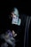 A person with light-colored hair holds a tarot card labeled 'Judgement' in a dimly lit setting. The person's arm and hand are heavily tattooed, and they are seated in a dark, studded chair.