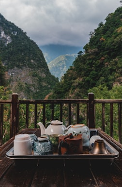 A rustic wooden table set with steaming bowls of Himalayan dishes surrounded by mountain scenery.
