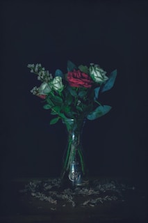 A moody still life featuring dark burgundy roses beside a perfume bottle, set against a charcoal backdrop.