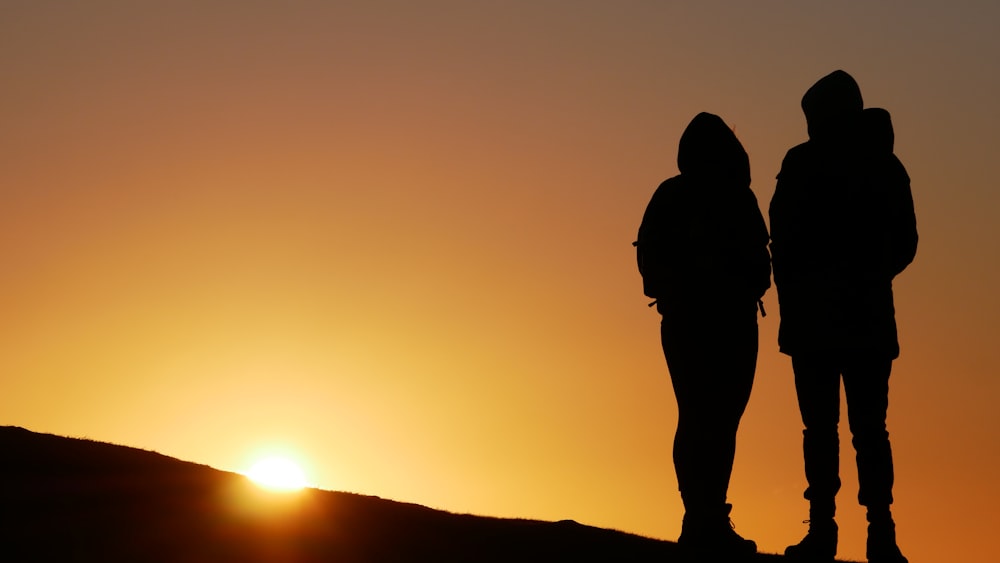 silhouette de personnes au sommet de la colline pendant le coucher du soleil