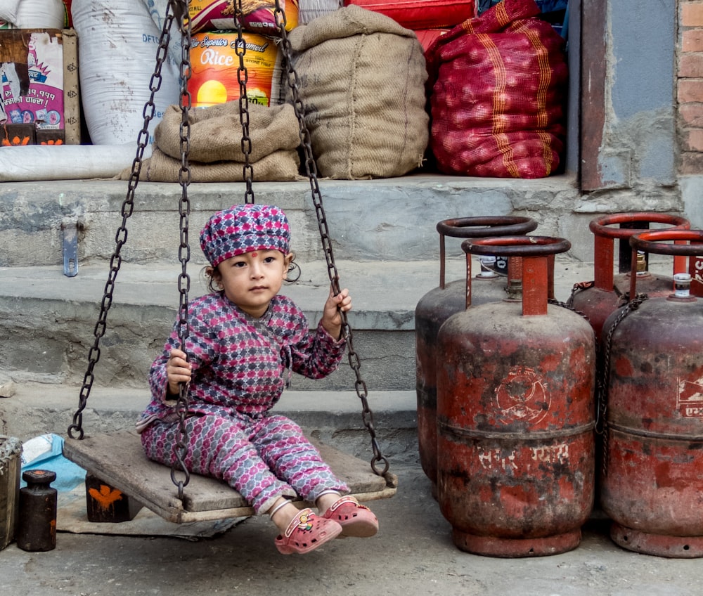 girl sitting on swing near cylinder tanks