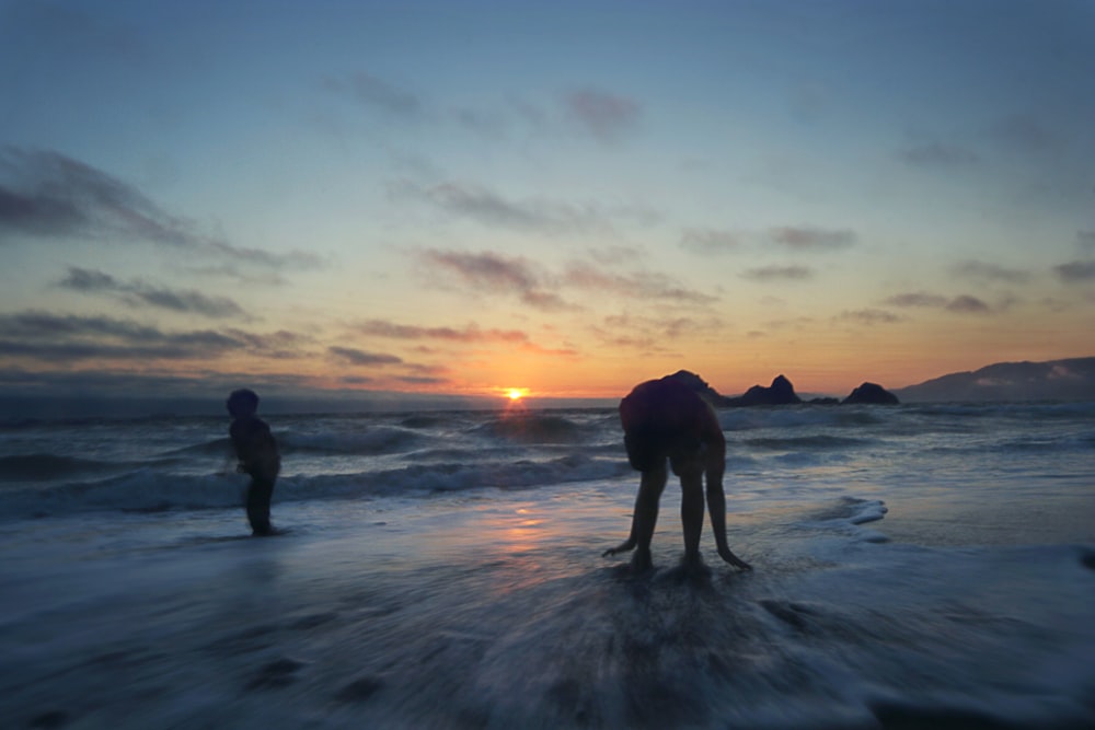 Dos personas de pie en el océano durante la puesta del sol