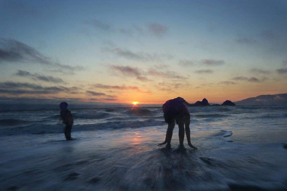 two people standing on ocean during sunset