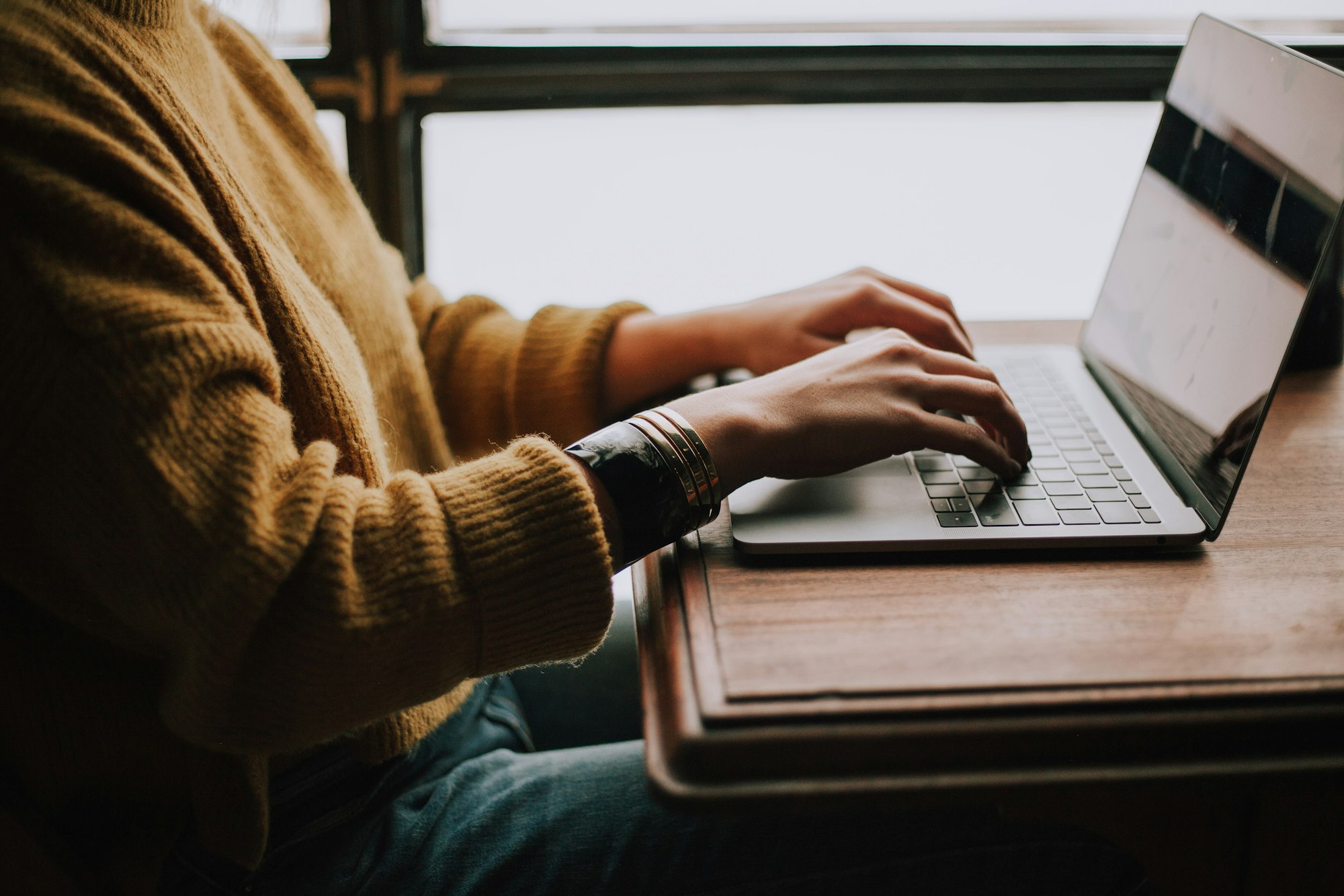 Woman wearing yellow sweater typing on her laptop