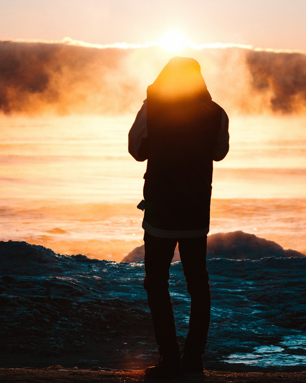 person standing on pavement facing body of water