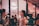 A stylish, indoor social gathering with people interacting in a lively atmosphere. The focus is on two individuals conversing, one holding a wine glass. The background features a Gogo Beauty sign and a wall adorned with photos. The ambiance is cozy and vibrant.
