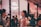 A stylish, indoor social gathering with people interacting in a lively atmosphere. The focus is on two individuals conversing, one holding a wine glass. The background features a Gogo Beauty sign and a wall adorned with photos. The ambiance is cozy and vibrant.