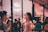 A stylish, indoor social gathering with people interacting in a lively atmosphere. The focus is on two individuals conversing, one holding a wine glass. The background features a Gogo Beauty sign and a wall adorned with photos. The ambiance is cozy and vibrant.