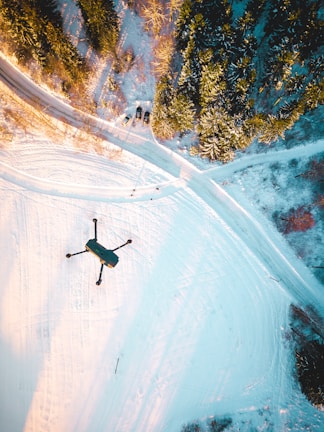black quadcopter drone flying over snow field during daytime