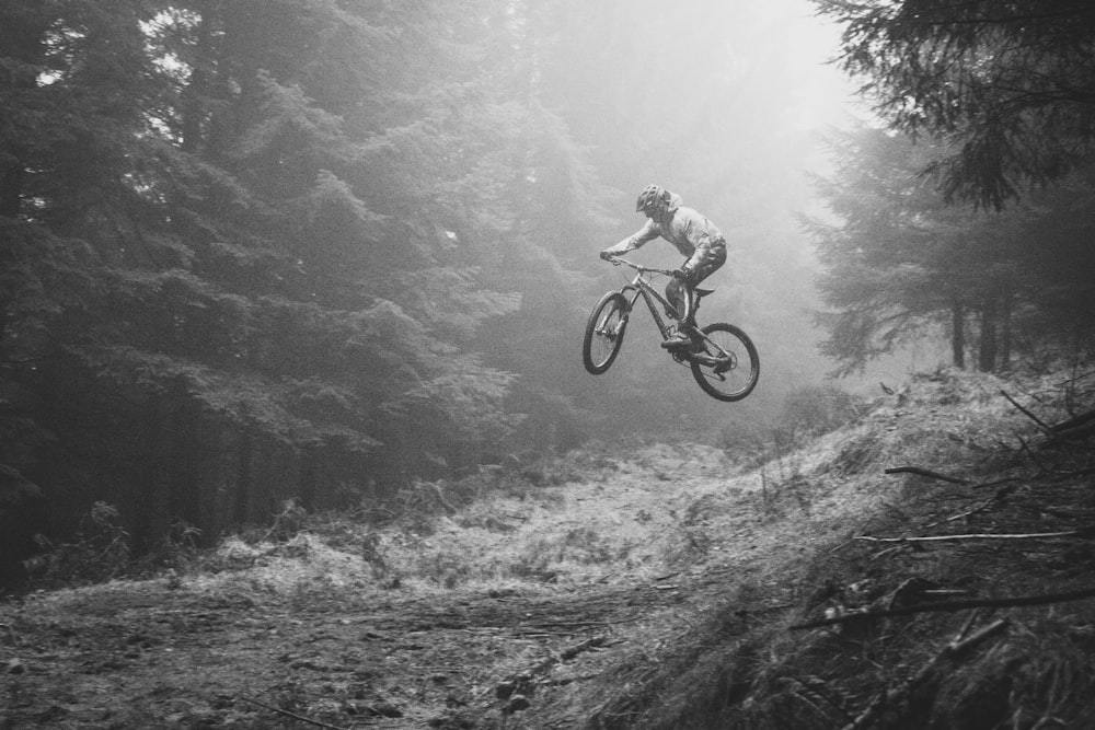 fotografia in scala di grigi di una persona che va in bicicletta nella foresta