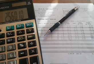 Close-up of hands signing a vehicle financing contract with legal documents and a calculator nearby.