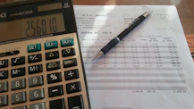 Close-up of hands typing on a calculator with mortgage documents nearby.
