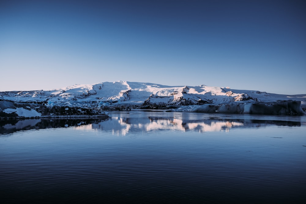 body of water near mountains covered with snow