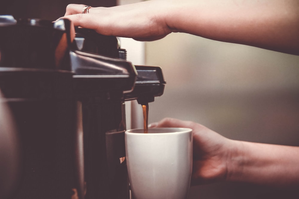 person using coffeemaker with white ceramic mug