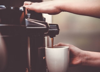 person using coffeemaker with white ceramic mug