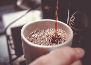 person holding white cup pouring coffee