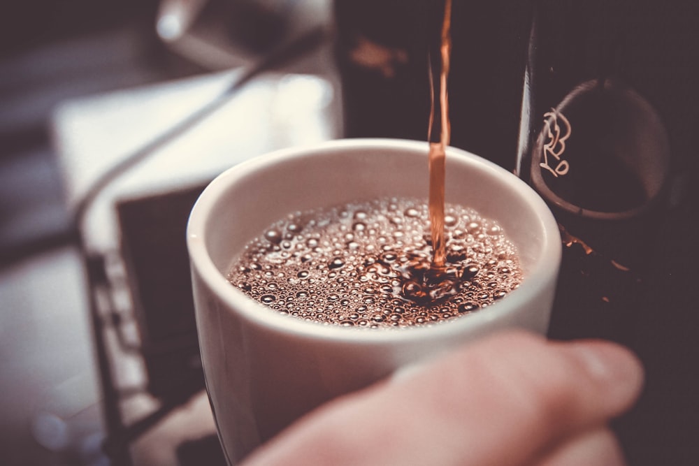 Persona che tiene la tazza bianca che versa il caffè