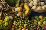 A vibrant assortment of tropical fruits arranged in baskets and piles at a market. The image features ripe bananas, papayas, oranges, melons, kiwis, and other fresh produce, creating a colorful and lively display.