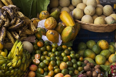 A vibrant assortment of tropical fruits arranged in baskets and piles at a market. The image features ripe bananas, papayas, oranges, melons, kiwis, and other fresh produce, creating a colorful and lively display.