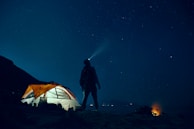 man standing beside camping tent wearing headlamp during nighttime