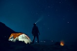 man standing beside camping tent wearing headlamp during nighttime
