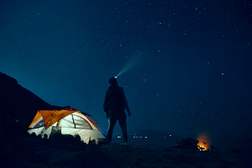 man standing beside camping tent wearing headlamp during nighttime