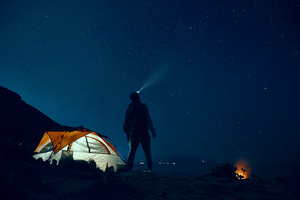 uomo in piedi accanto alla tenda da campeggio che indossa la lampada frontale durante la notte