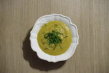 A vibrant green pea soup served in a minimalist bowl, adorned with microgreens and a sprinkle of cracked black pepper.
