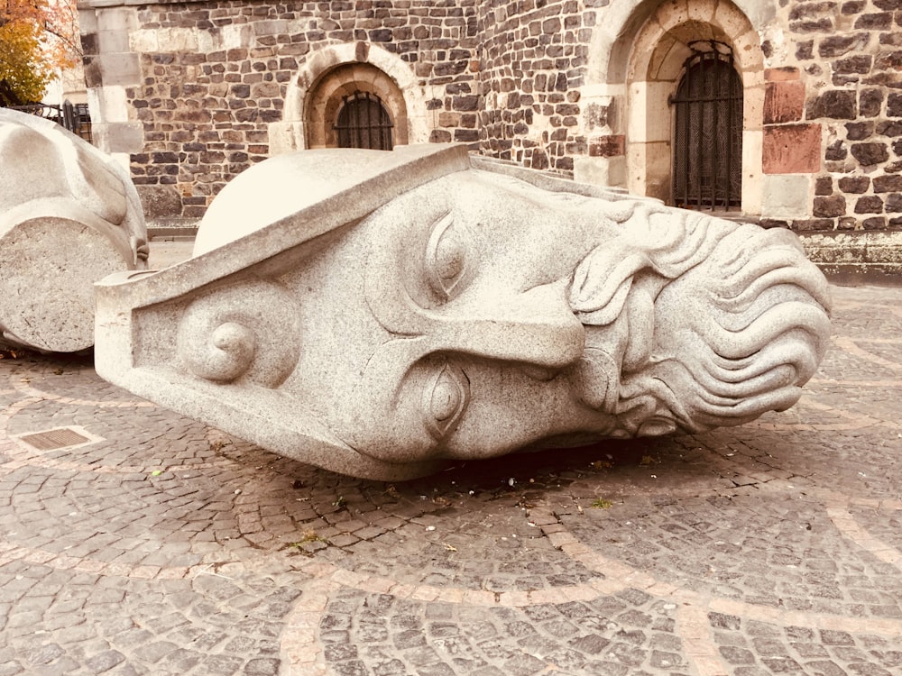 a stone sculpture of a head on a cobblestone street