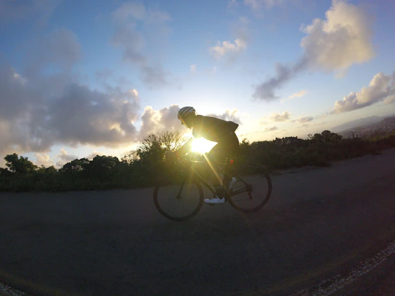 Sunset casting warm light over a winding trail with a cyclist silhouetted in the distance.