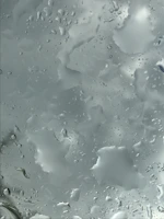 Close-up of water droplets sliding off a freshly cleaned glass surface reflecting the blue sky.