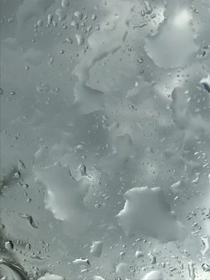 Close-up of water droplets sliding off a freshly cleaned glass surface reflecting the blue sky.