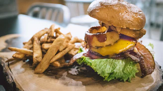 The Qarmashoo burger served with a side of golden fries on a rustic wooden board.