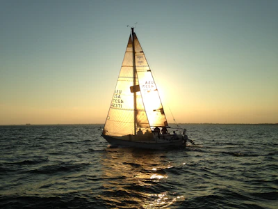 Golden hour shot of a family laughing aboard a sailboat, sails softly glowing in the warm light.