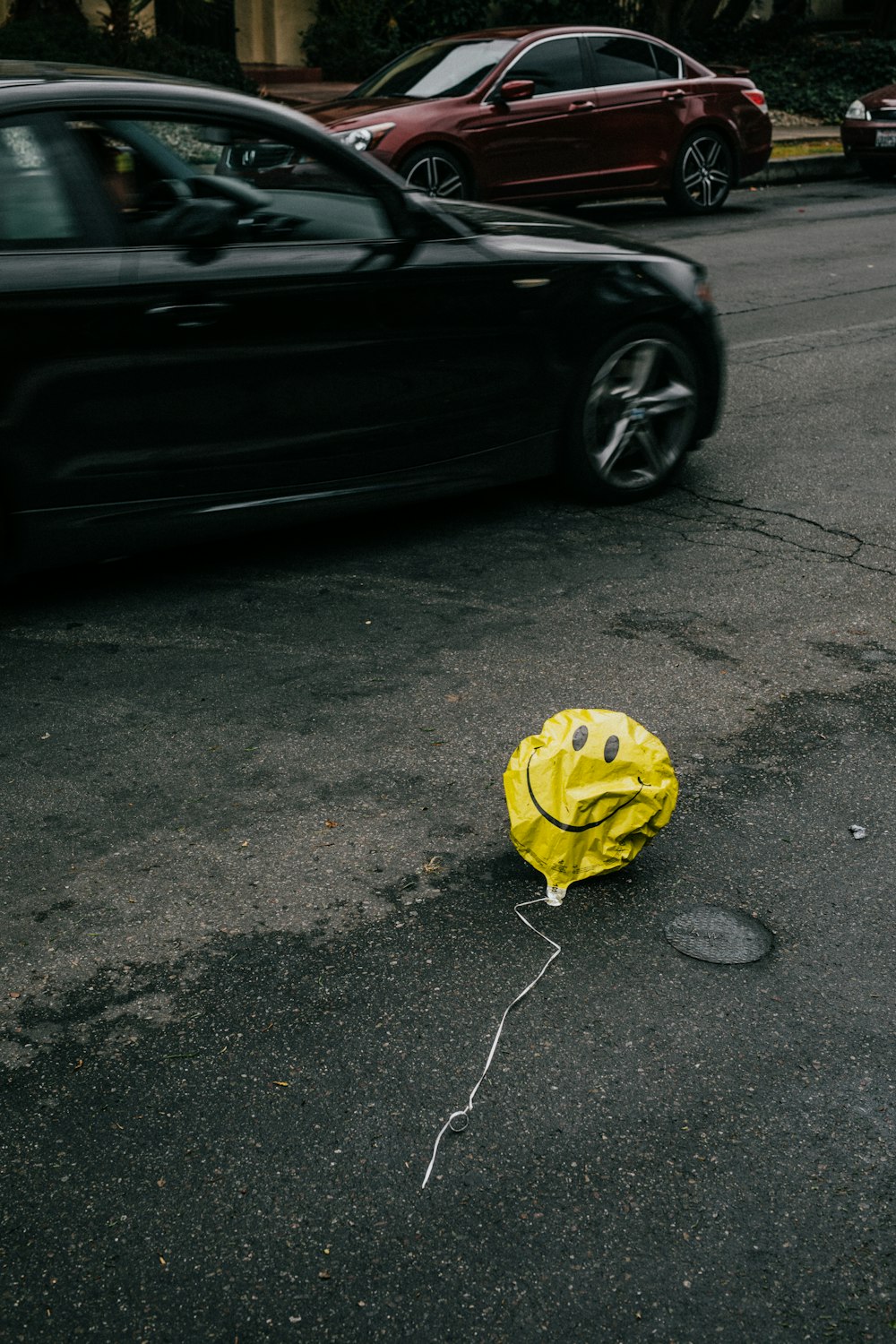 smiling emoji balloon beside black car during daytime
