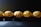 Five chocolates wrapped in crinkled golden foil are lined up against a dark background, with light casting a subtle shine on the wrappers.