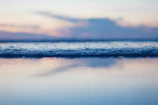 A minimalist seascape with calm waves and a pastel sky at dusk.
