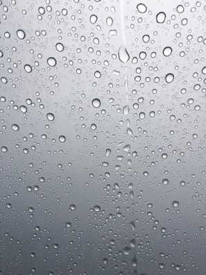 Filtered water droplets on a smooth glass surface reflecting soft blue tones.