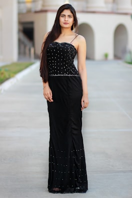 Model wearing a flowing black evening dress against a minimalist urban backdrop.