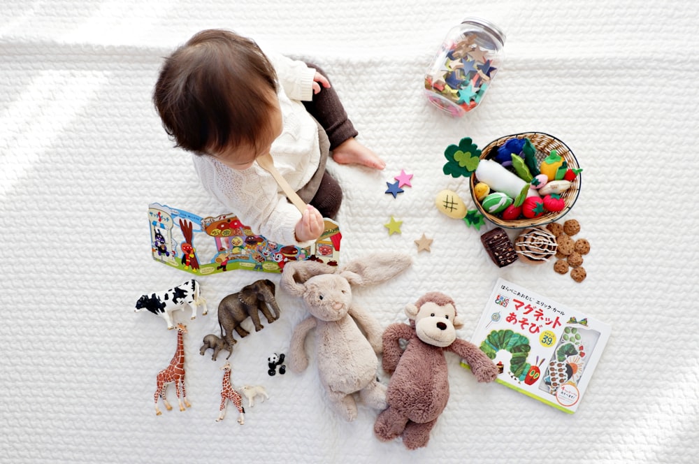 Junge sitzt auf weißem Tuch, umgeben von Spielzeug