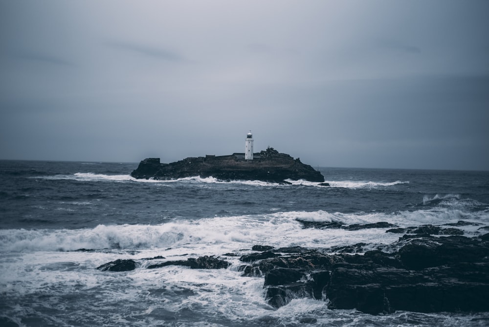 white lighthouse on rock formation surrounded by ocean