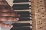 A close-up of hands playing on a piano keyboard, showcasing both black and white keys. The mechanical components of the piano are visible, adding an intricate detail to the scene.