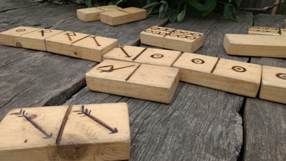 Wooden blocks with engraved symbols are scattered on a rustic wooden surface. The symbols appear handcrafted and vary from circles to arrows and lines.
