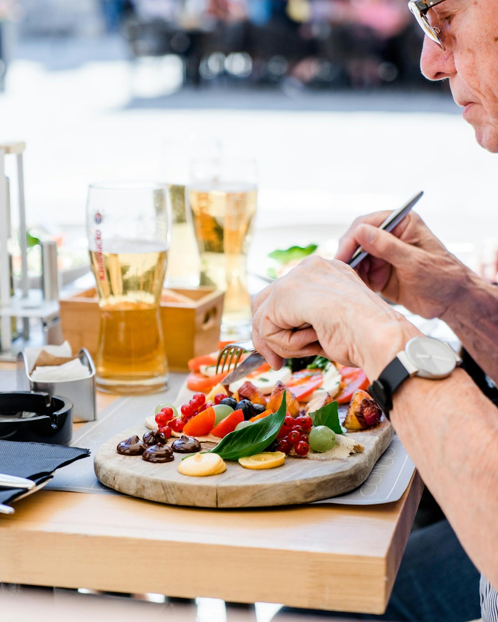 man slicing fruits on top of board beside drinking glass with yellow labeled liquid at daytime