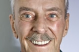 A close-up portrait of an elderly Allen with a warm, welcoming smile.