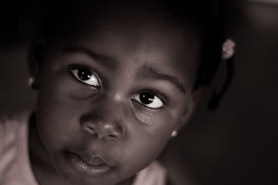 A close-up portrait of a young child gazing upwards. The image is in a sepia tone with soft lighting that emphasizes the child's expressive eyes. A subtle focus on the emotions conveyed through the child's facial expression.